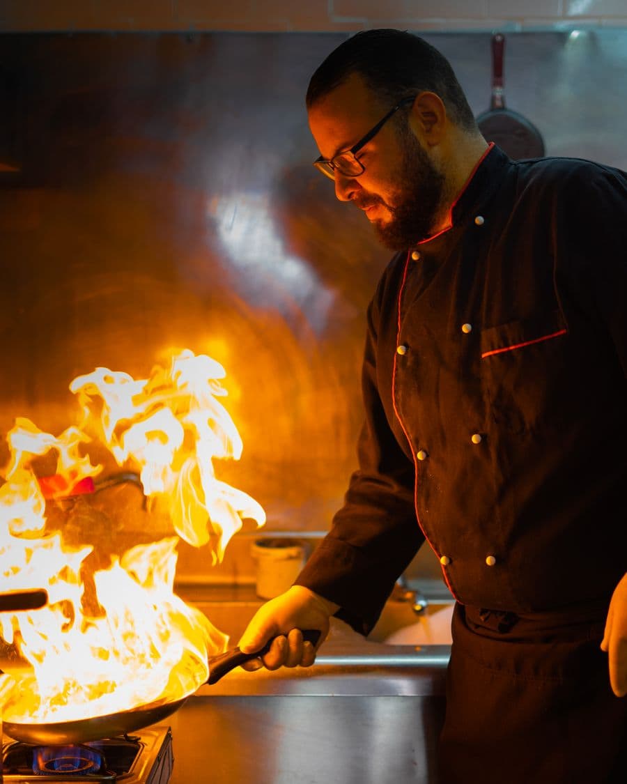Chef managing a dramatic flame flare-up over a pan in a professional kitchen