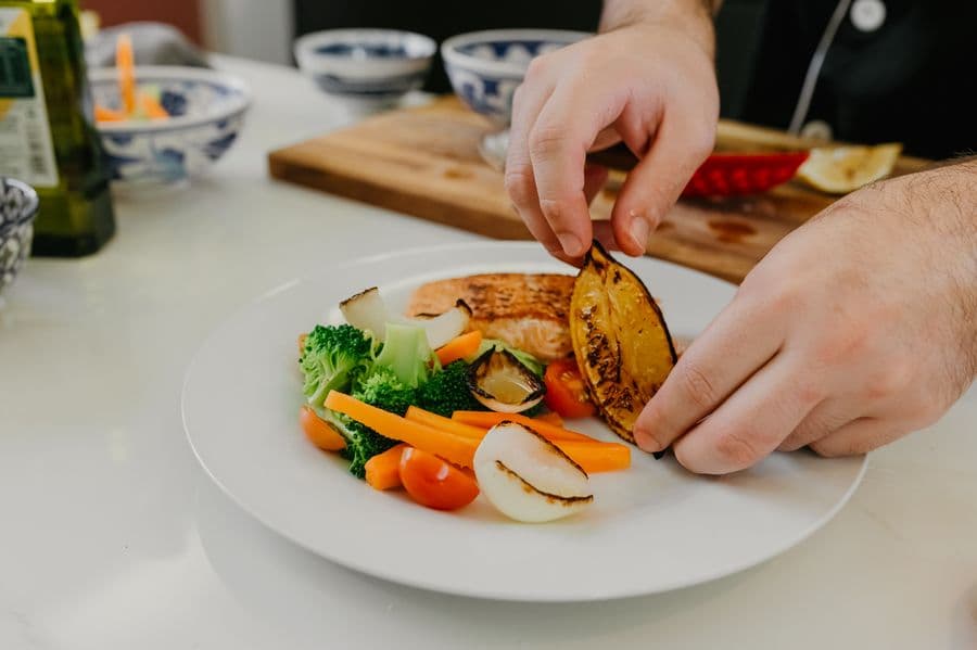 Chef carefully plating grilled salmon with fresh vegetables