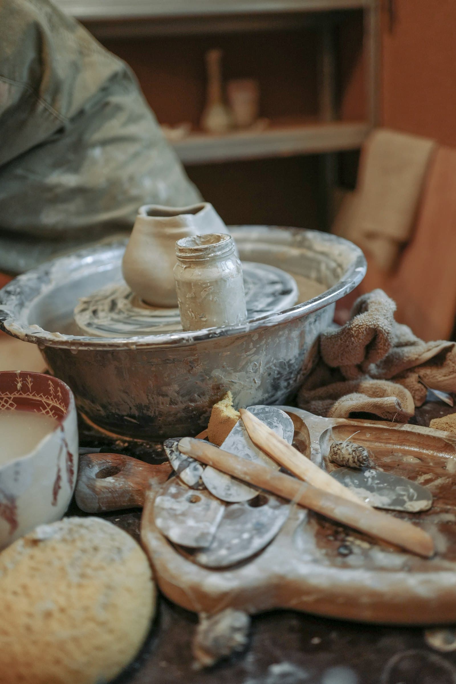 A potter's wheel surrounded by tools and finished ceramics in a studio